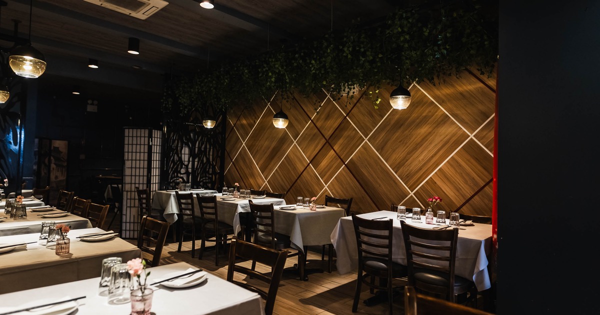 Interior, wide shot of a dining room, white cloth tables with wooden chairs, subtle lighting