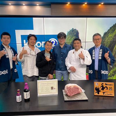 Six people pose smiling in a TV studio, In front, a table with bottles, certificate and meat  on it.