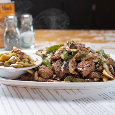 Steaming Cajun butter steak with mushrooms and peppers on a plate.