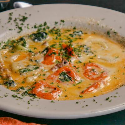 Bowl of tortellini soup with herb garnish.