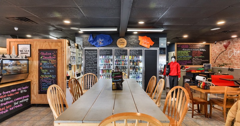 Casual interior dining area with a long wooden table close up, and glass-front refrigerators behind