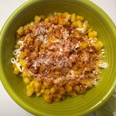 Bowl of Mexican street corn topped with spices and cheese.