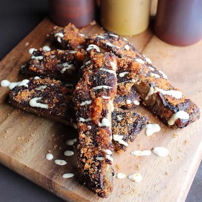 Fried ribs drizzled with sauce on a wooden board with condiments in the background
