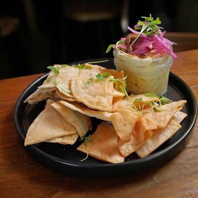 Seasonal hummus topped with pickled vegetables, served with chips.