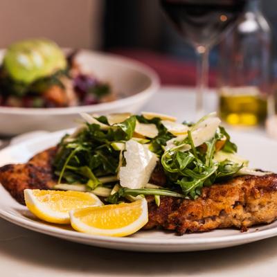 Breaded pork chop with arugula salad and lemon wedges.