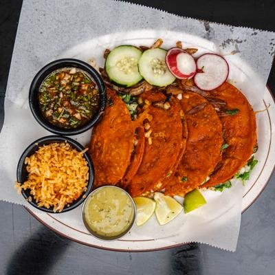 Birria tacos served with rice, consomme, dipping sauce, lime wedges and garnishes.