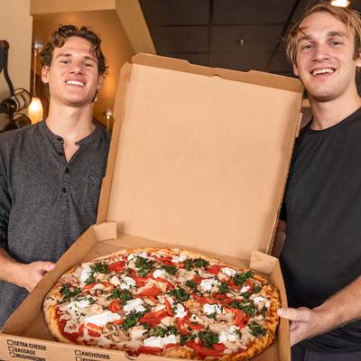 Inside, two staff members hold take-away box with chicken pizza