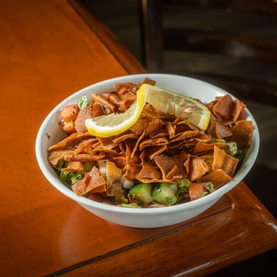 Pita Fattoush salad served in a white bowl on a wooden table.