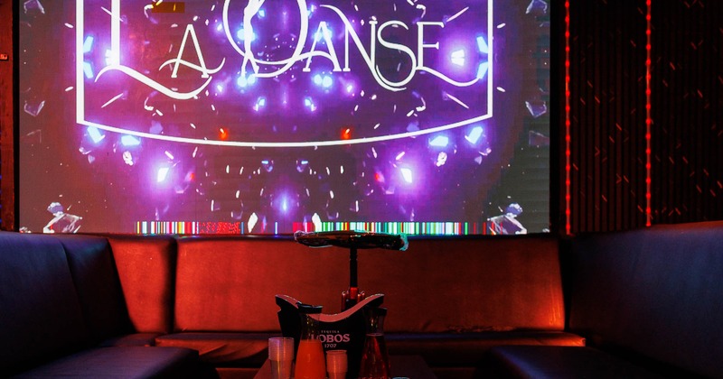 A lounge area - a screen displaying "LA DANSE" and a marble table surrounded by dark leather couches