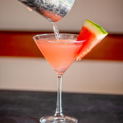 Watermelon martini garnished with a watermelon wedge, being strained into a glass.