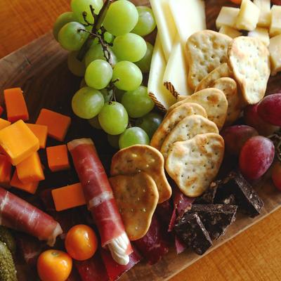 A charcuterie board with grapes, cheese, cured meat, crackers, pickles, tomatoes, and chocolate.