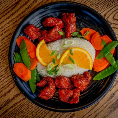 Plate with orange chicken, rice, and vegetables on a wooden table.