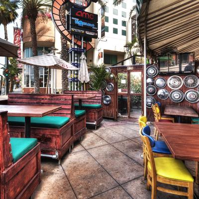 Outdoor seating area with wooden benches and green cushions, colorful chairs, and hubcap wall decor