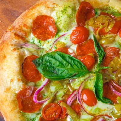 Pizza with cherry tomato, pepperoni, pesto sauce, mozzarella, close up