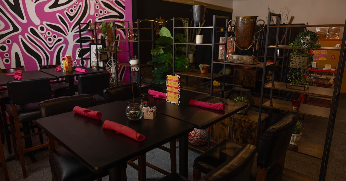 Interior, dark wooden tables, rolled red napkins, abstract wall mural, decorative shelving units