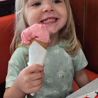 Adorable little girl with a big smile eating a strawberry ice cream cone..