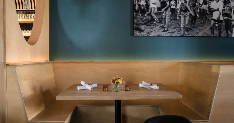Restaurant booth with a wooden table, a teal wall and black-and-white photo
