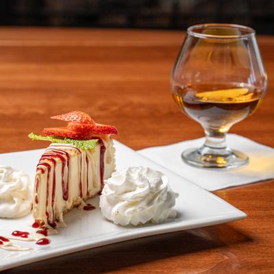 New York Style Cheesecake served on the table alongside a glass of spirit.