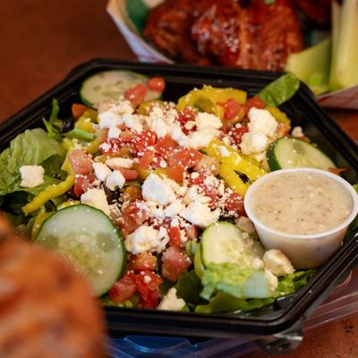 Greek salad packed in a black takeout container with a small container of dressing.