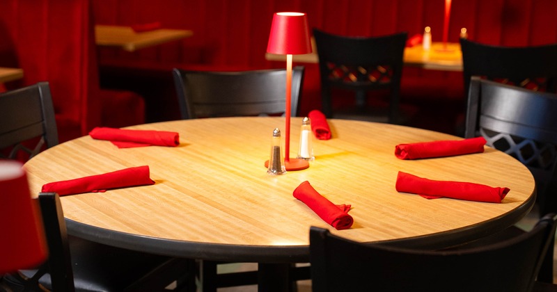 Round wooden table with red napkins and small lamp in a restaurant setting