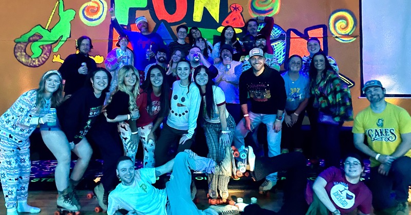 A large group of people pose together at a roller skating rink