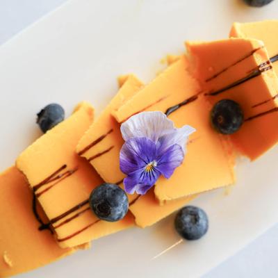 Mango dessert garnished with chocolate drizzle, blueberries, and a violet flower.