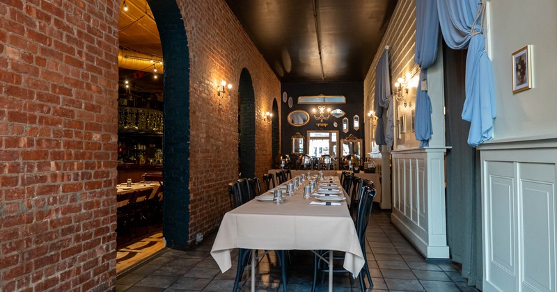 A restaurant dining room with a long table set for a meal, surrounded by a brick wall
