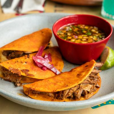 Quesabirria tacos served with pickled onion, consome and a lime wedge.