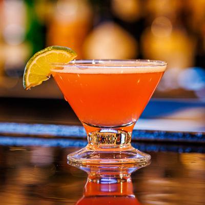 The Cosmo cocktail, garnished with lime, resting on a bar counter.