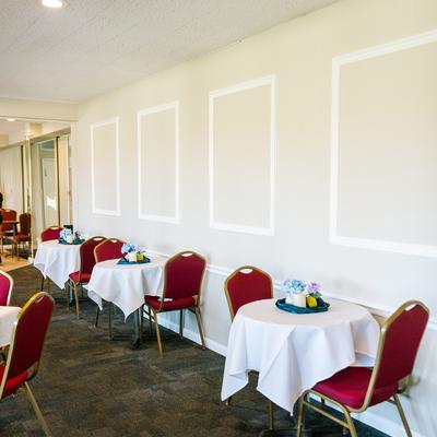 A room with white walls, white tablecloths on tables, floral display  and red chairs.