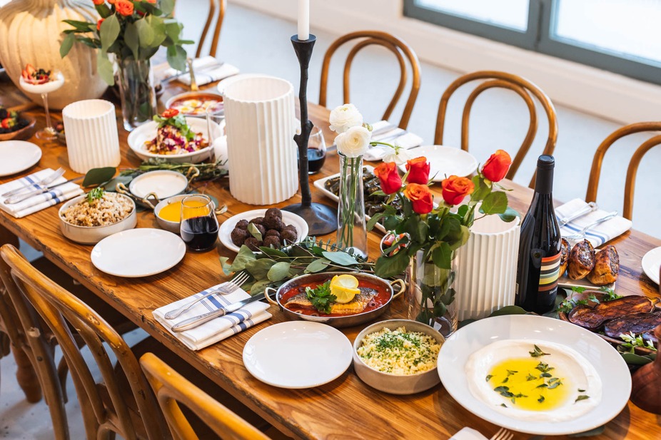 A beautifully arranged table with food plates, bowls, candles and flowers as the centerpiece