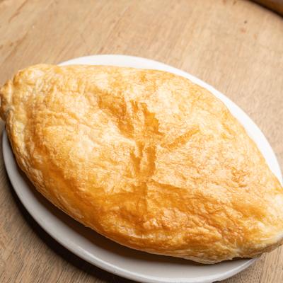 Golden calzone on a white plate over a wooden table.