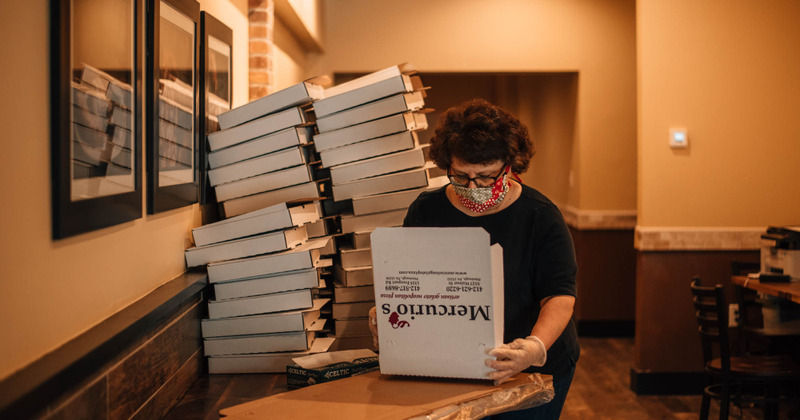 An employee assembling a pizza box by the table with stacks of boxes