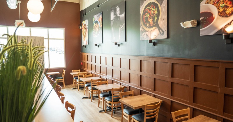 Interior of a restaurant with wooden tables and chairs, hanging lights, and food images on the wall