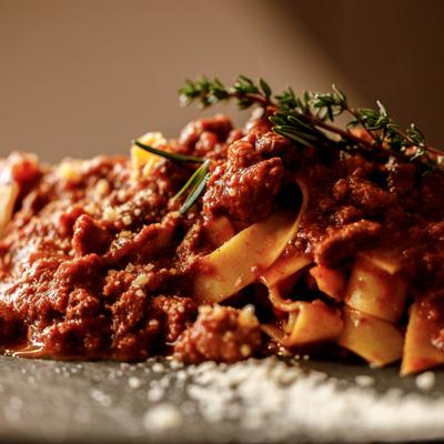 Close-up of tagliatelle with meat sauce and rosemary on a plate.