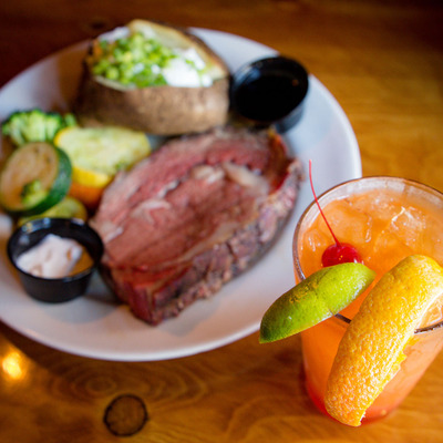 Orange cocktail in the foreground and a steak dish in the background