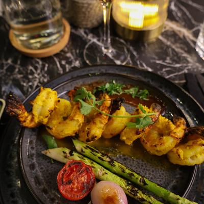 Tandoori Mango Shrimp garnished with herbs, and served alongside grilled vegetables.