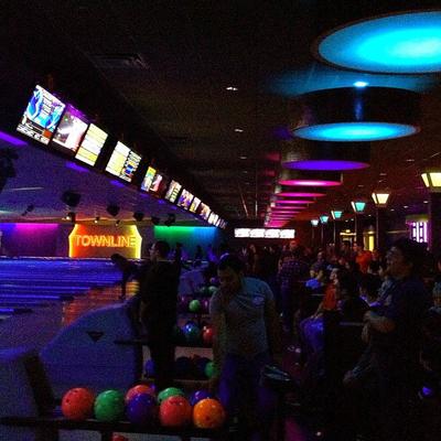 A vibrant neon-lit bowling alley features crowded lanes and colorful bowling balls.