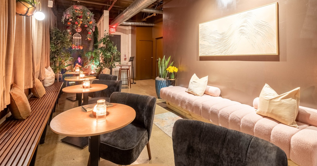 Cozy lounge with wooden tables, pink bench seating, and decorative plants under warm lighting