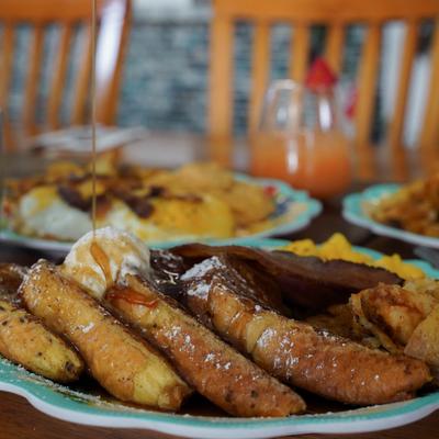 Syrup being drizzled over French toast with butter and powdered sugar.