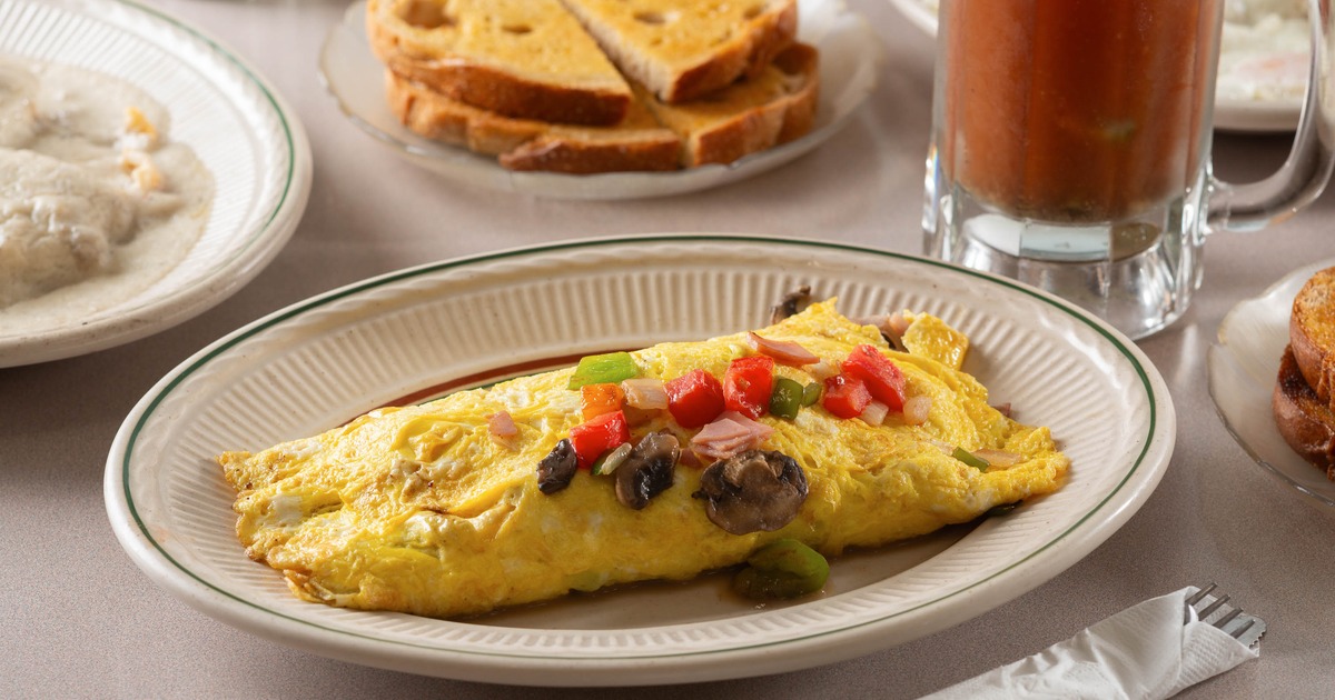 Omelet topped with peppers mushrooms and tomatoes beside toast