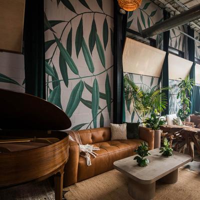 Stylish interior area featuring a piano, comfortable couch, various indoor plants, leaf mural.