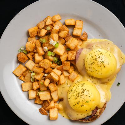 Eggs Benedict topped with hollandaise sauce and served with breakfast potatoes.