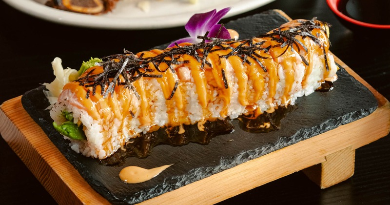 A specialty sushi roll with orange sauce, nori, and an orchid