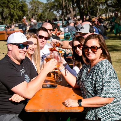 A group of people toast with drinks at a table outside.