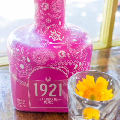 A bottle of cream tequila and a glass with a flower in it.