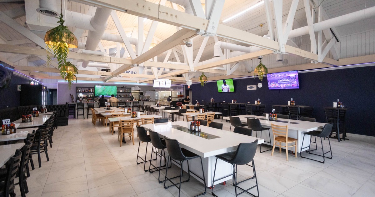 Modern restaurant interior with high ceilings, white tables, black and wood chairs
