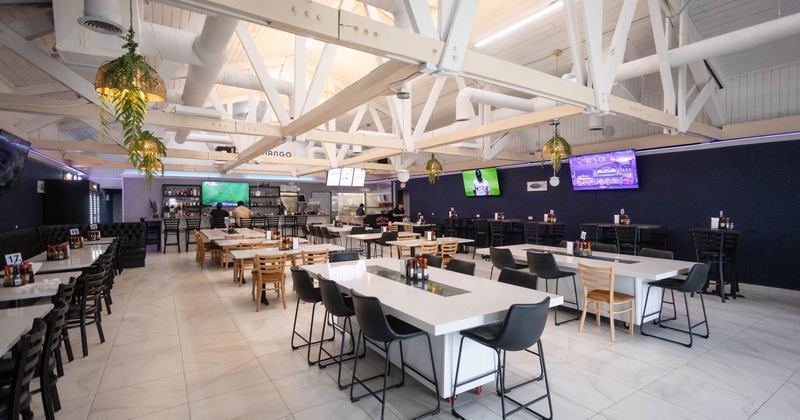 Modern restaurant interior with high ceilings, white tables, black and wood chairs