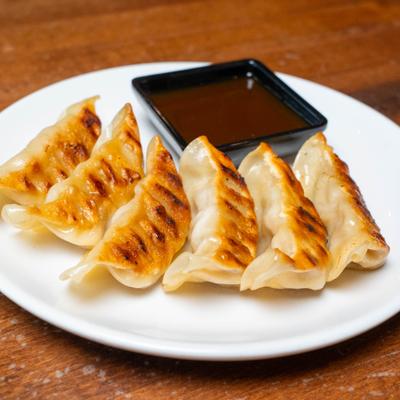 Pan-fried dumplings served with ponzu sauce on a white plate.