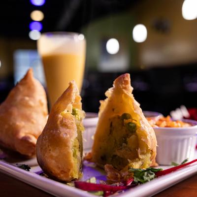 Three samosas on a plate with a drink in the background.